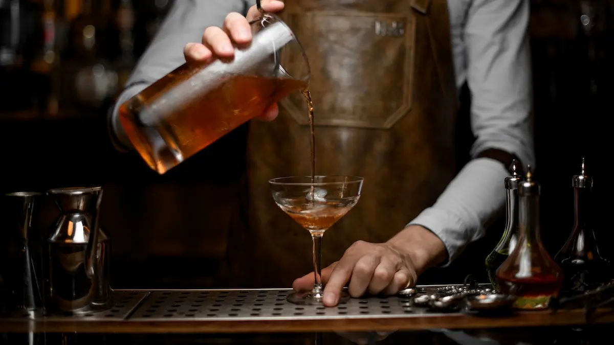 bartender pouring a drink into a martini class